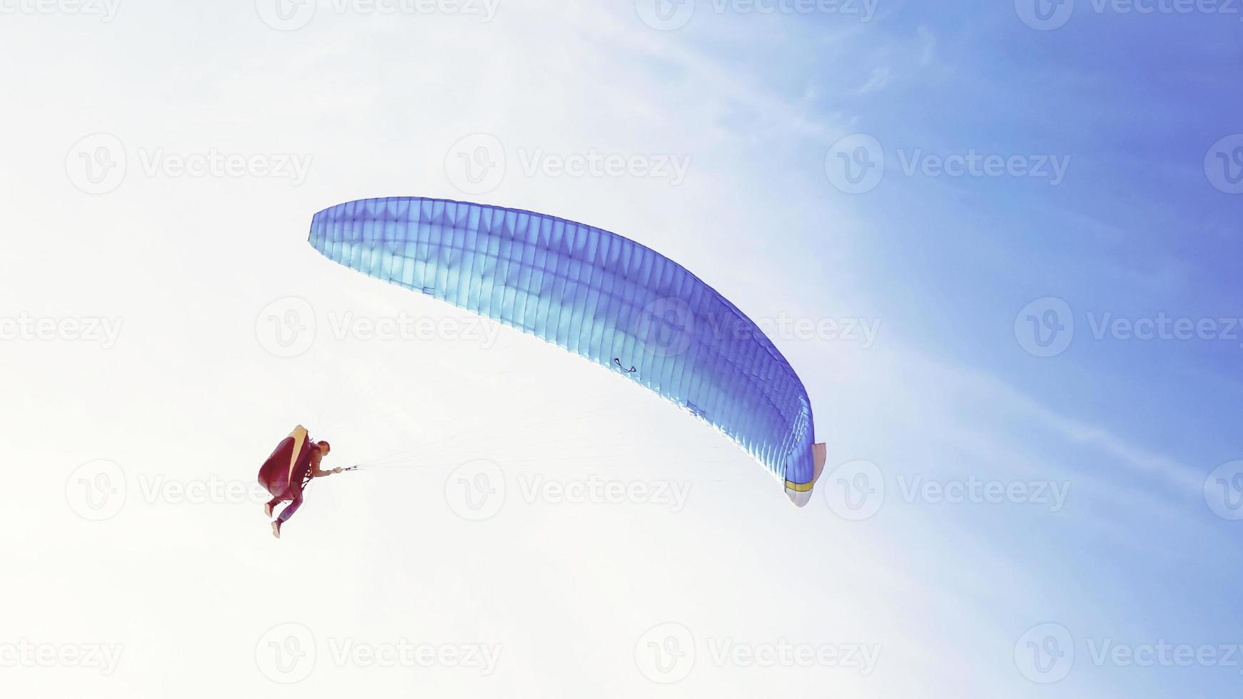 paraglider with blue wing flying in blue sky photo