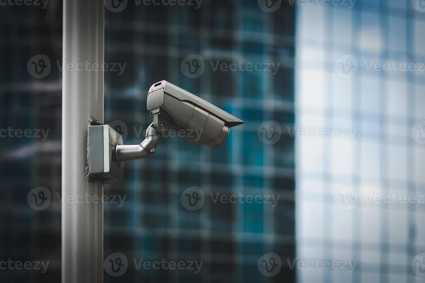 External security camera on pole in front of glass building wall photo
