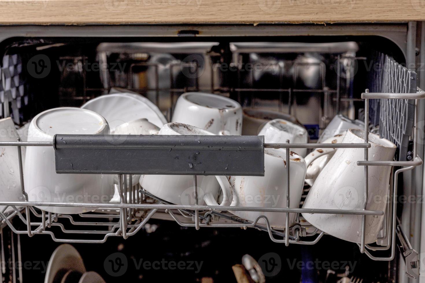 Unwashed, dirty dishes in dishwasher. Mess in the kitchen. Dirty kitchenware, plates and mugs. Messy dishware. Close up view. photo