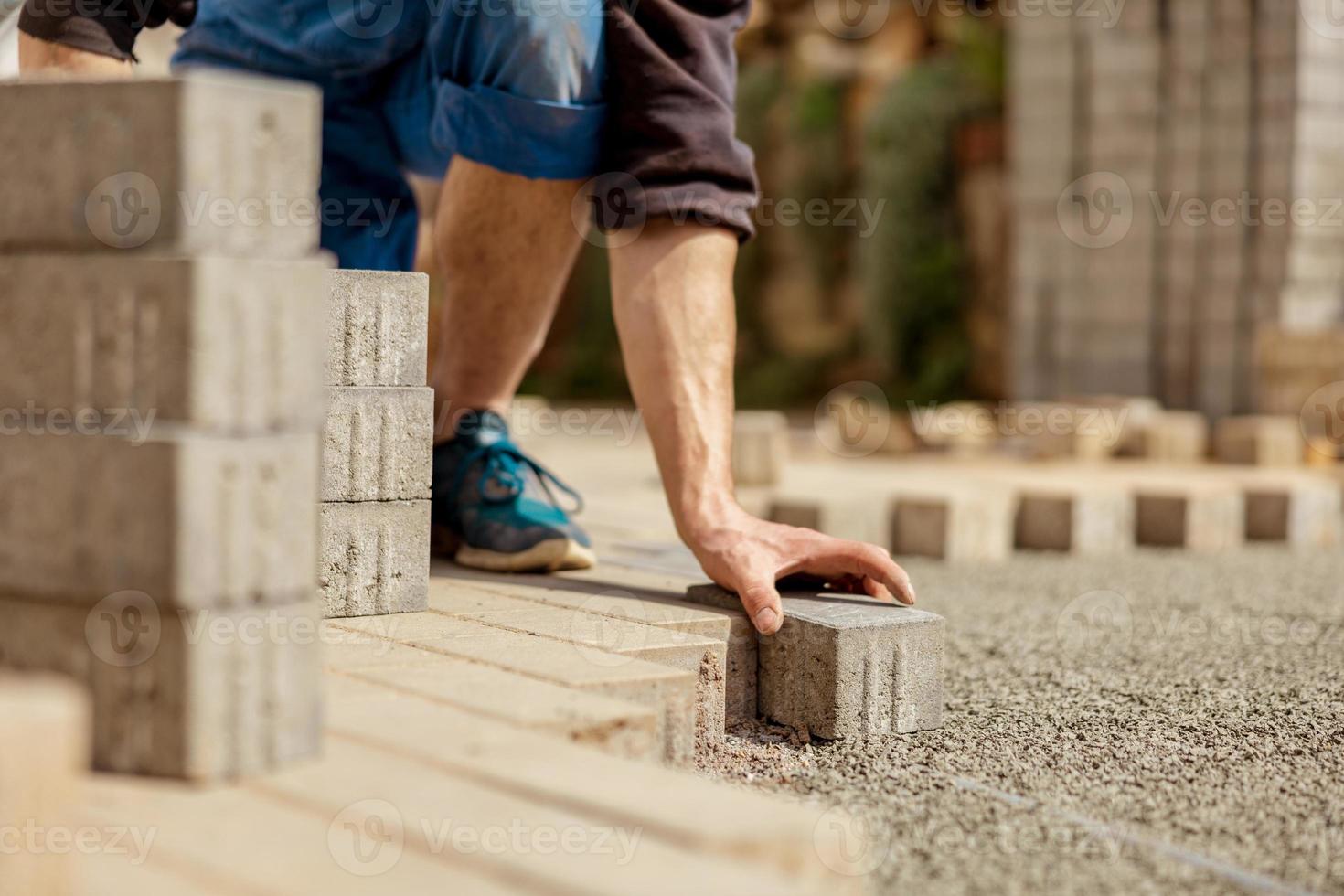 Young man laying gray concrete paving slabs in house courtyard on gravel foundation base. Master lays paving stones. Garden brick pathway paving by professional paver worker. Repairing sidewalk. photo