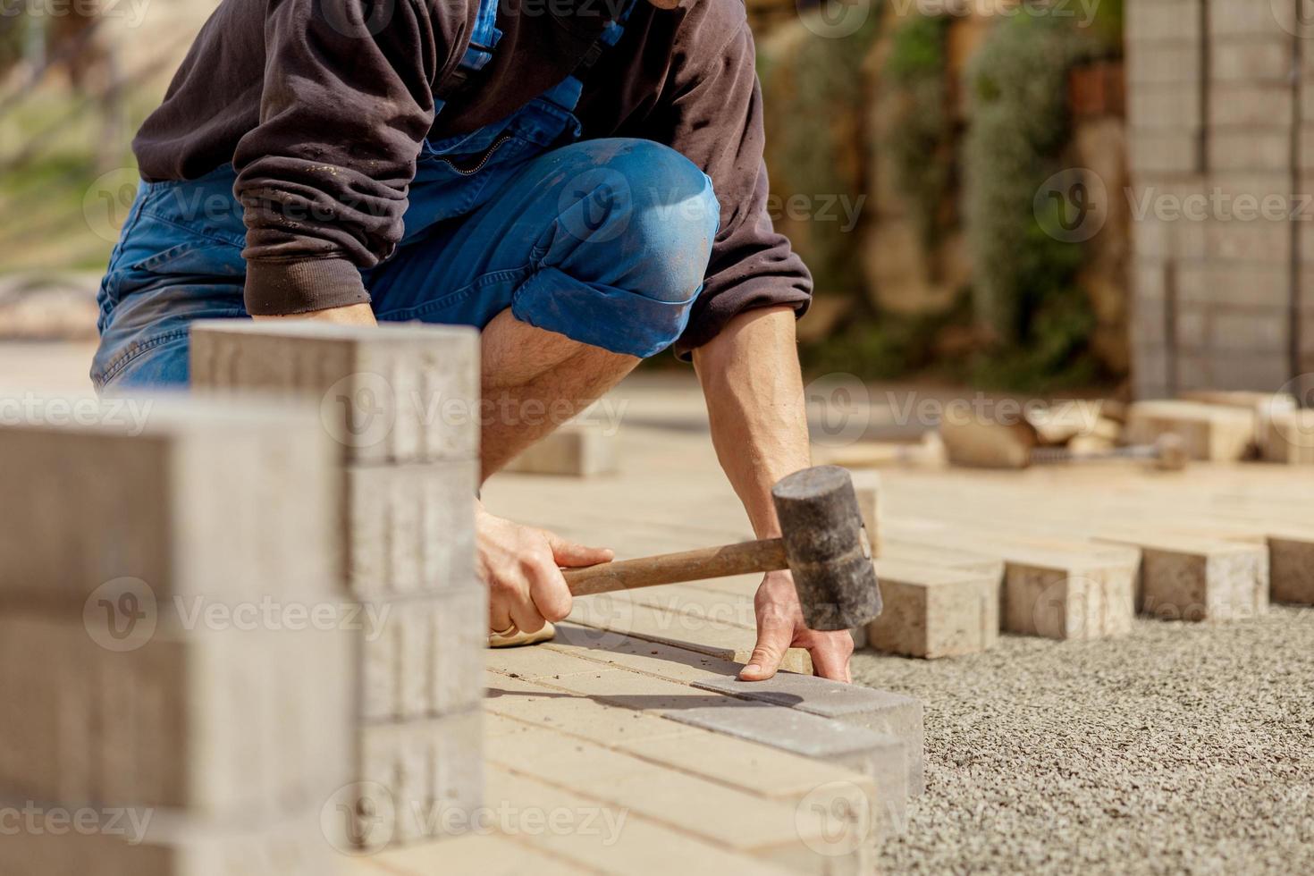 joven colocando losas de hormigón gris en el patio de la casa sobre la base de la base de grava. el maestro pone adoquines. pavimentación de caminos de ladrillos de jardín por un trabajador profesional de pavimentadoras. reparación de acera. foto