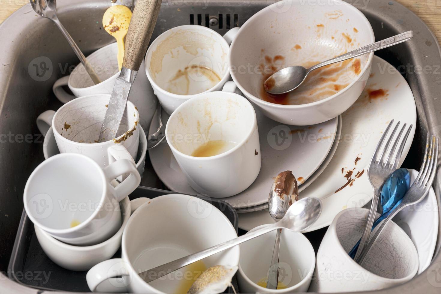 Pile of unwashed, dirty dishes in the sink. Mess in the kitchen. Dirty kitchenware, plates and mugs. Chaos at home. Laziness. Cluttered apartment. Messy cutlery and dishware. photo