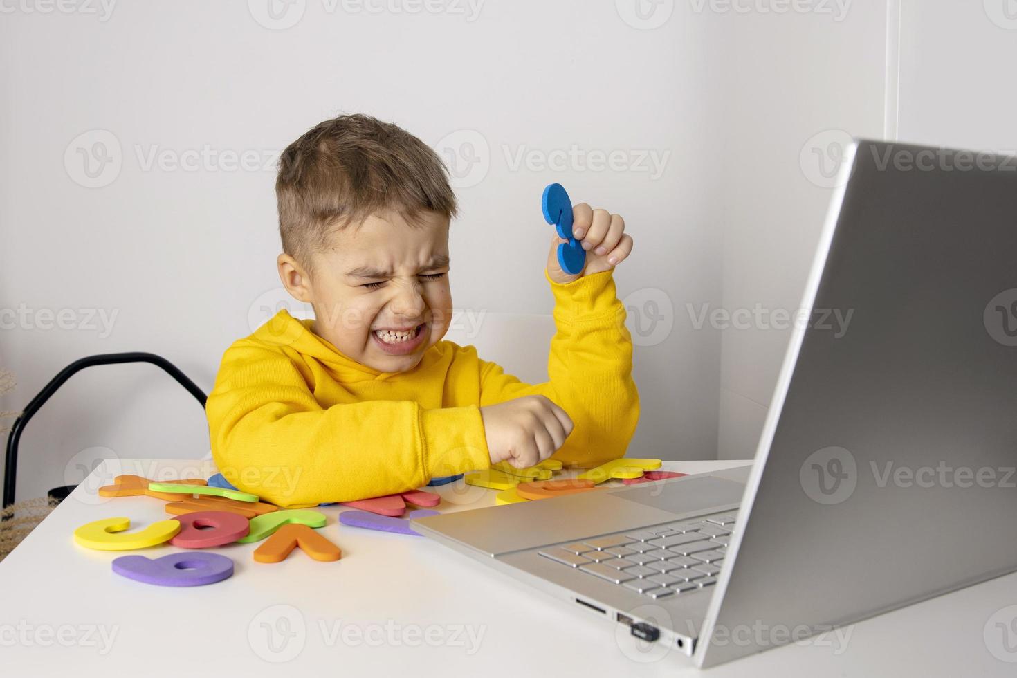 niño pequeño aprendiendo alfabeto y números en línea, con computadora portátil en casa. el niño está triste y estresado. emociones negativas, ira, estrés, problemas mentales. educación en el hogar y educación a distancia para niños. foto