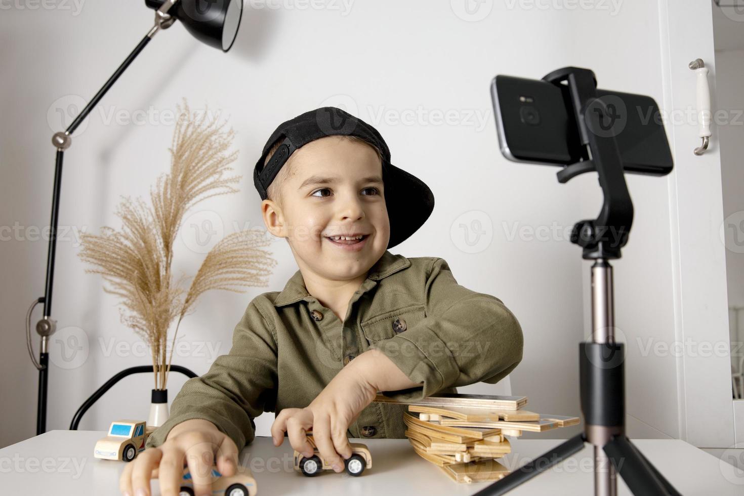 Adorable, cute, little boy blogger recording lifestyle blog, talking to camera of smartphone on tripod. Young influencer filming vlog for his channel. Child makes video for his followers online. photo