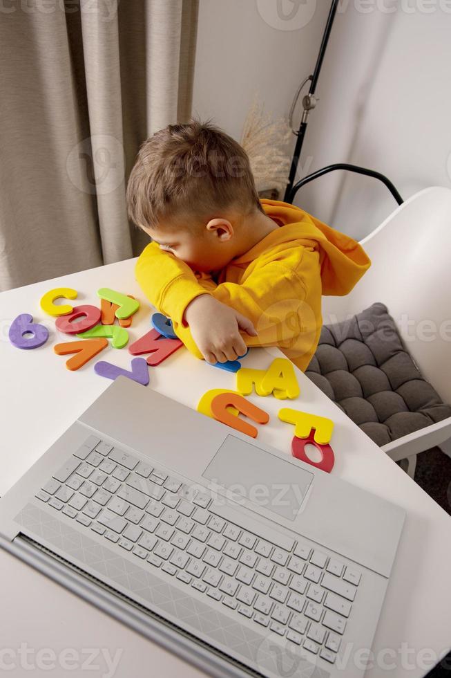 Little boy learning alphabet and numbers online, with laptop at home. Child is sad and tired. Negative emotions, stress, mental problems. Homeschooling and distance education for kids. photo