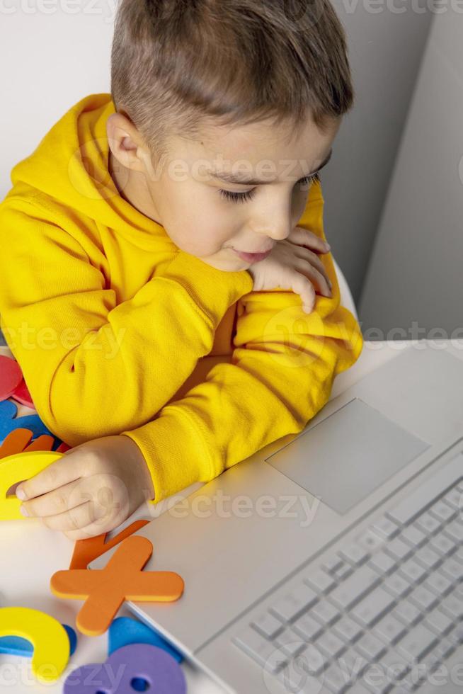 Adorable, cute, little boy learning alphabet online, with laptop at home. Child using e-learning platform to make a video call with his teacher and study. Homeschooling and distance education for kids photo