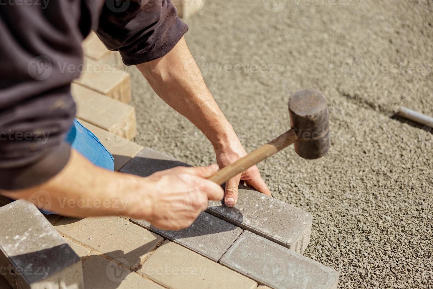 Young man laying gray concrete paving slabs in house courtyard on gravel foundation base. Master lays paving stones. Garden brick pathway paving by professional paver worker. Repairing sidewalk. photo