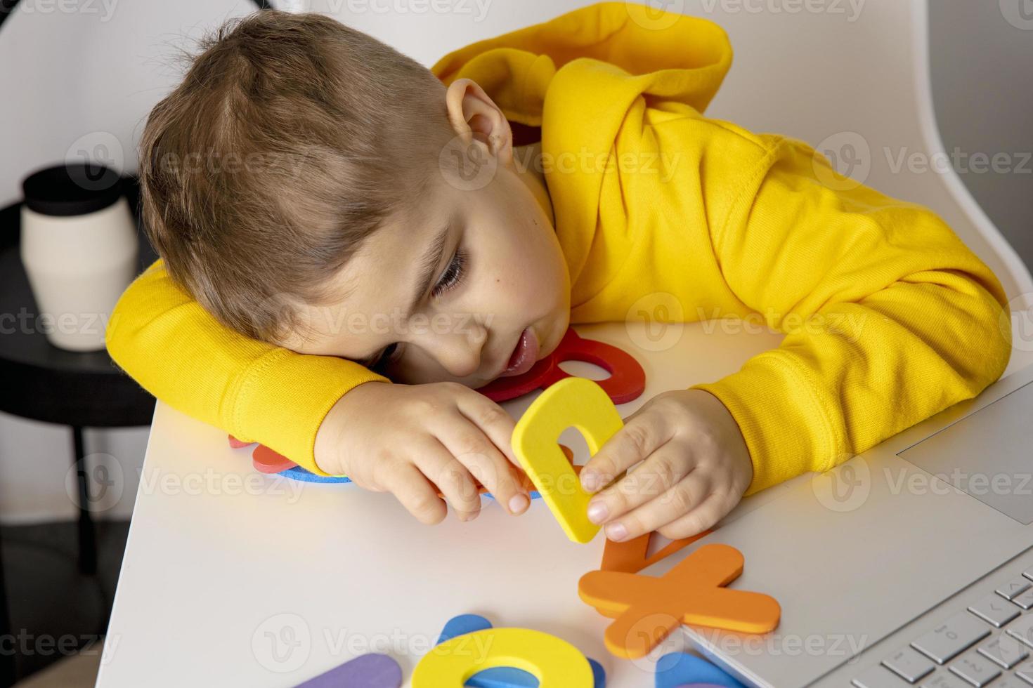 Little boy learning alphabet and numbers online, with laptop at home. Child is sad and tired. Negative emotions, stress, mental problems. Homeschooling and distance education for kids. photo