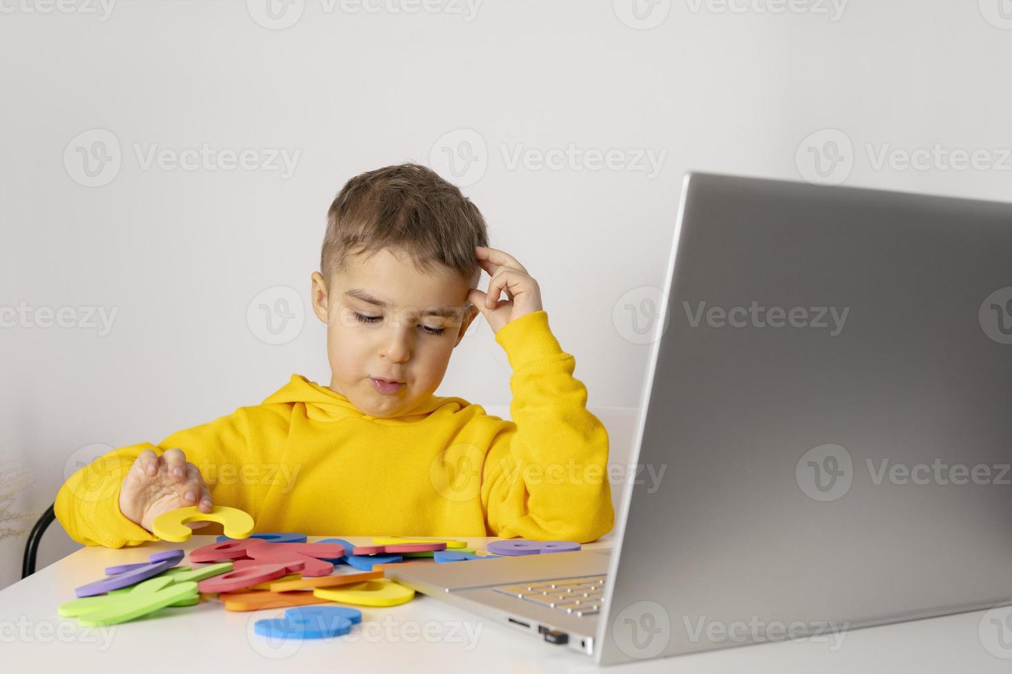 Adorable, cute, little boy learning alphabet online, with laptop at home. Child using e-learning platform to make a video call with his teacher and study. Homeschooling and distance education for kids photo