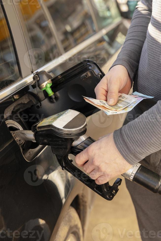 Car refuelling on petrol station. Man refilling car with fuel and holding money, euros. Close up. Gasoline, diesel is getting more expensive. Petrol industry and service. Petrol price and oil crisis. photo