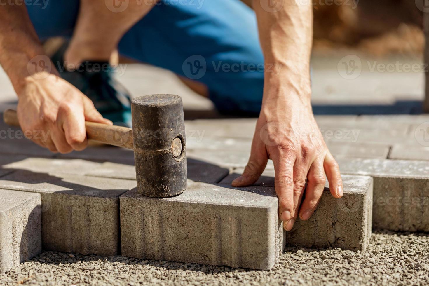 joven colocando losas de hormigón gris en el patio de la casa sobre la base de la base de grava. el maestro pone adoquines. pavimentación de caminos de ladrillos de jardín por un trabajador profesional de pavimentadoras. reparación de acera. foto