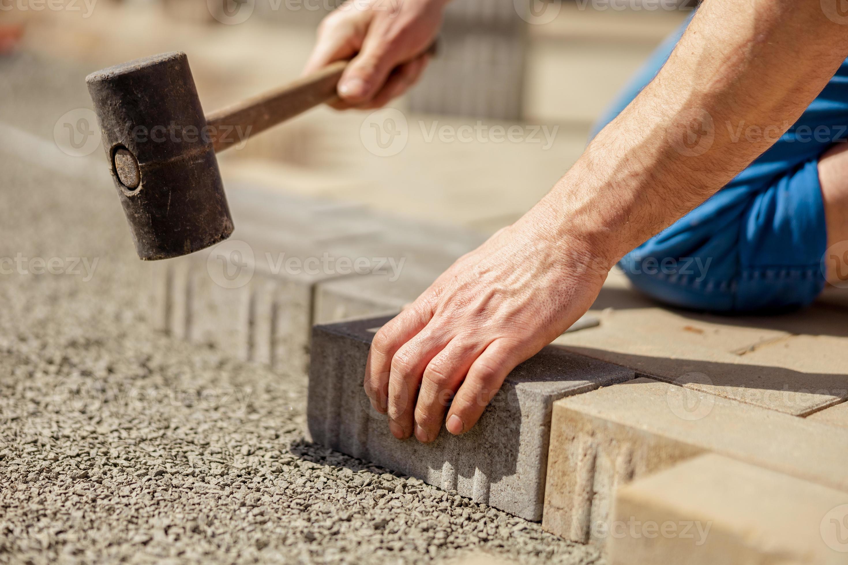 Young man laying gray concrete paving slabs in house courtyard on