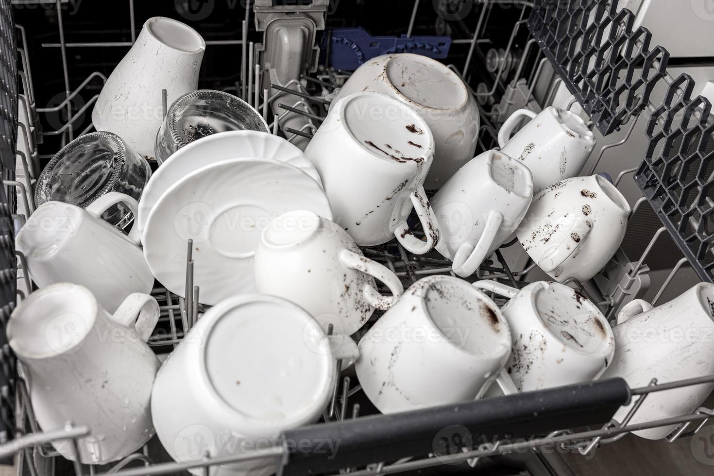 platos sin lavar y sucios en el lavavajillas. desorden en la cocina. utensilios de cocina, platos y tazas sucios. vajilla desordenada. vista de cerca foto