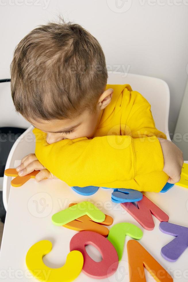 Little boy learning alphabet at home. Child is tired and sad. Homeschooling and distance education for kids. Negative emotions. photo