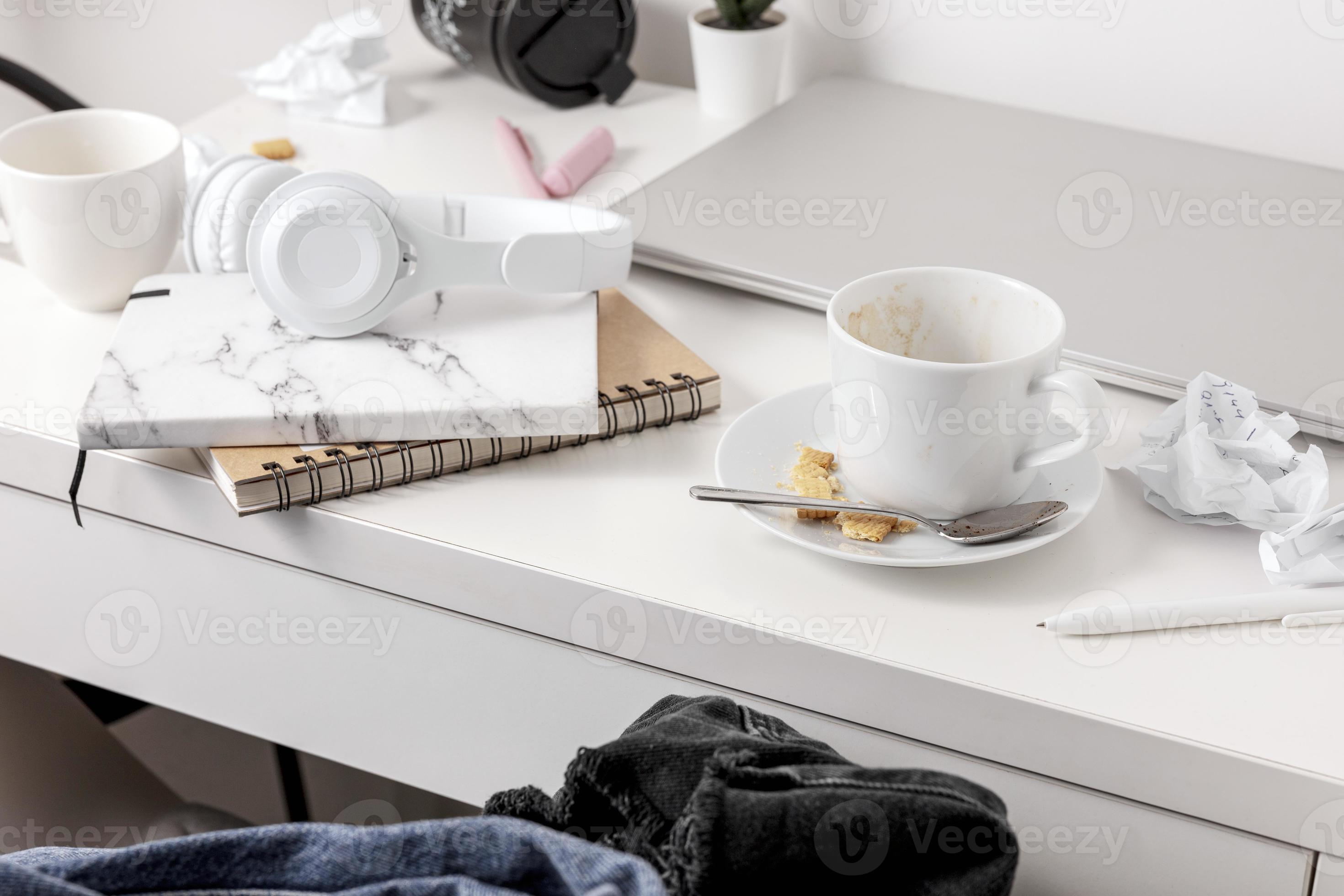 Messy table with laptop, dirty cups, and stationary items. Cluttered
