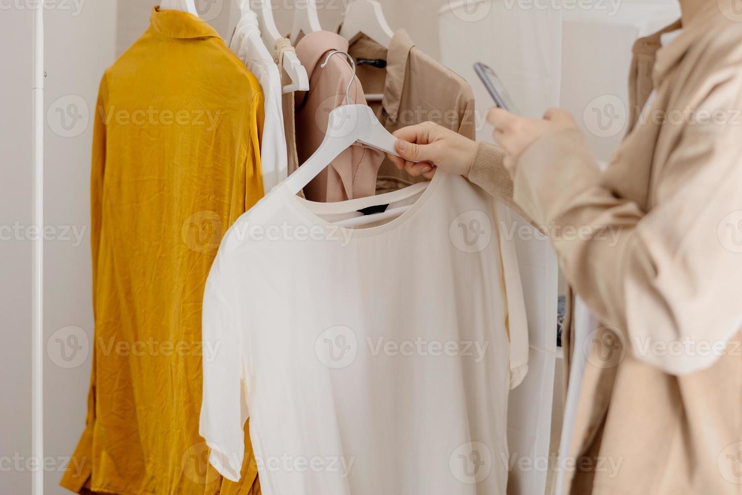 mujer sosteniendo un teléfono inteligente y tomando fotos de su ropa vieja para venderla en línea. venta en sitio web, comercio electrónico. reutilización, concepto de segunda mano. consumidor consciente, estilo de vida sostenible. vista de primer plano