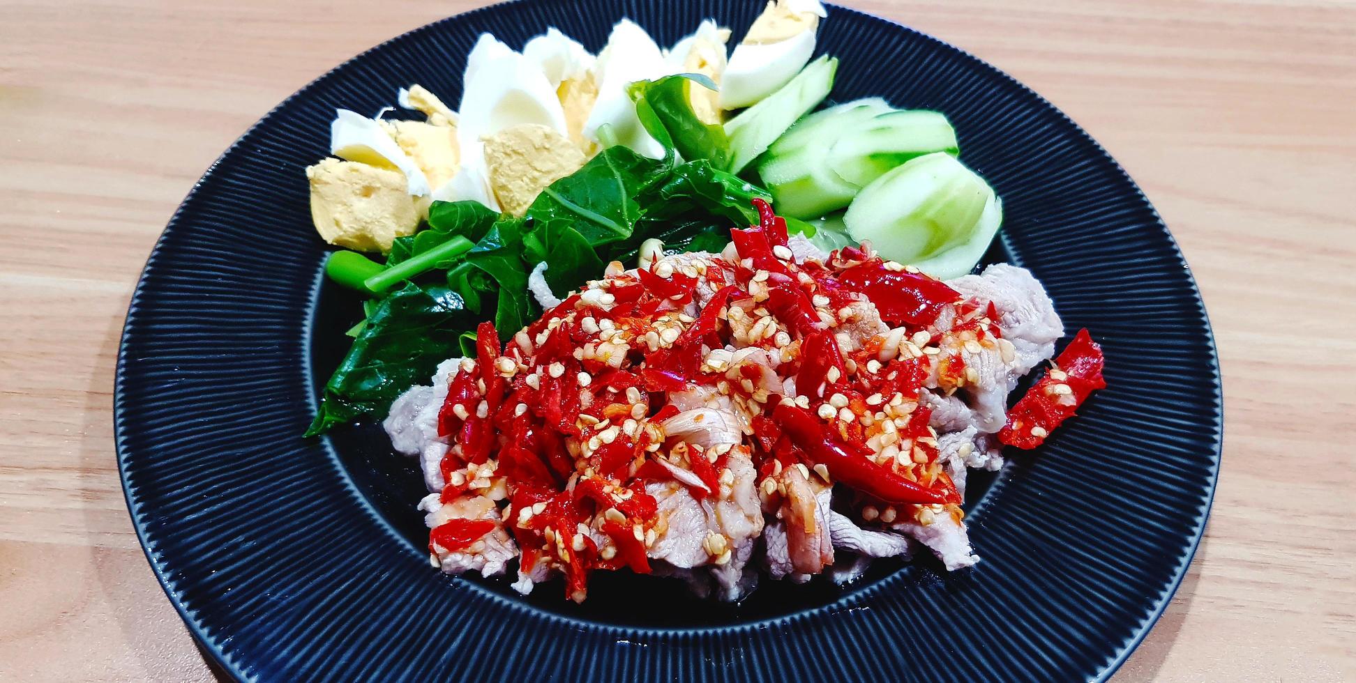 Boiled pork with lime, garlic and red chili sauce on black dish. Spicy food with beef, sliced boiled egg, cucumber and kale on plate . Delicious meal in Thai style and Healthy eating life. photo