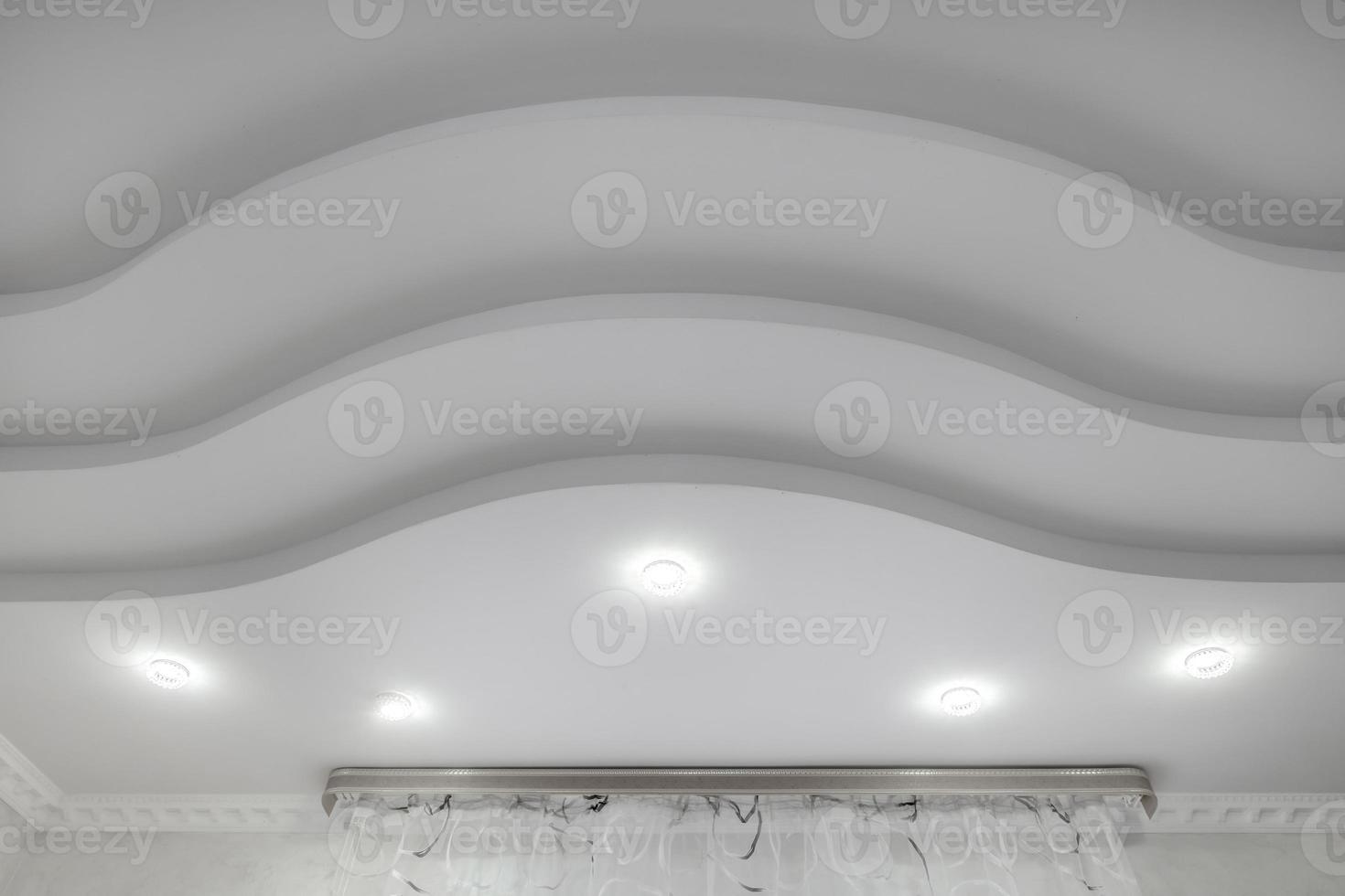 suspended ceiling with halogen spots lamps and drywall construction  with intricate crown molding in empty room in apartment or house. Stretch ceiling white and complex shape. photo