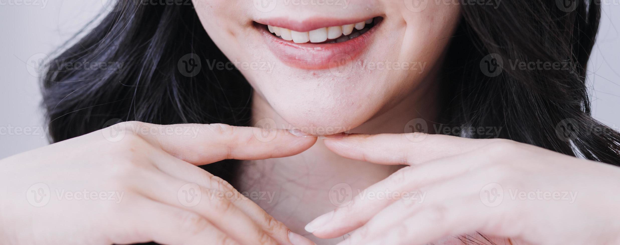 concepto de estomatología, retrato parcial de una chica con fuertes dientes blancos mirando la cámara y sonriendo, con los dedos cerca de la cara. primer plano, de, mujer joven, en, dentista, estudio, adentro foto