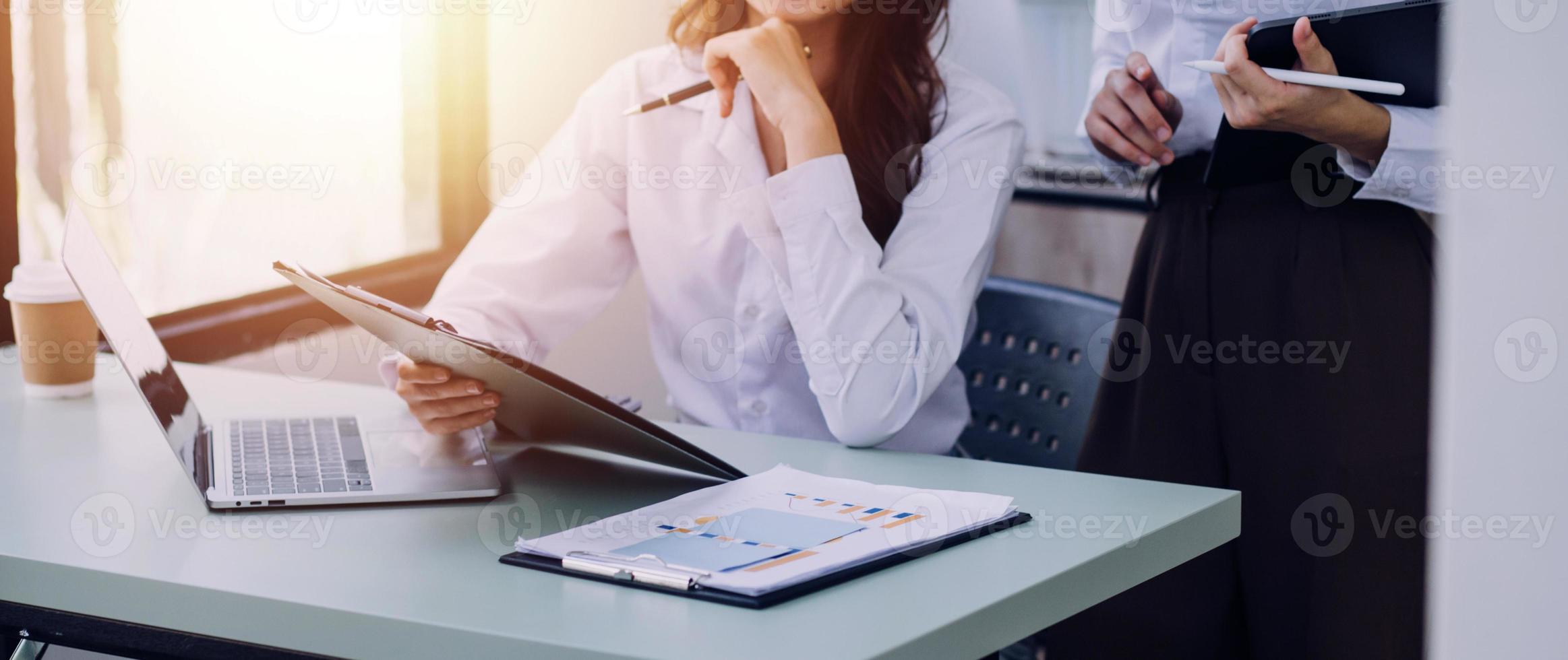 Young business woman sitting in office at table and using smartphone. On desk is laptop and tablet computer, on screen charts and graphs. Woman analyzing data. Student learning online. photo