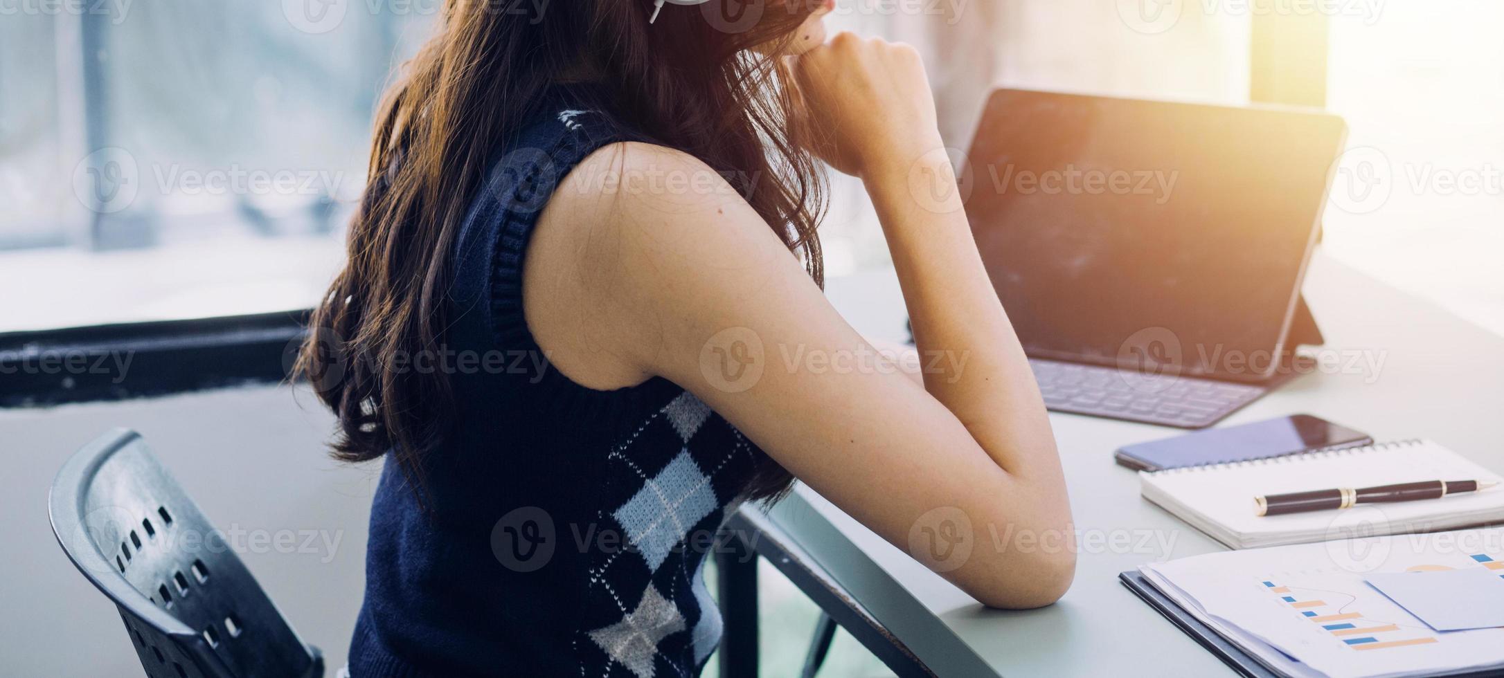 Young business woman sitting in office at table and using smartphone. On desk is laptop and tablet computer, on screen charts and graphs. Woman analyzing data. Student learning online. photo