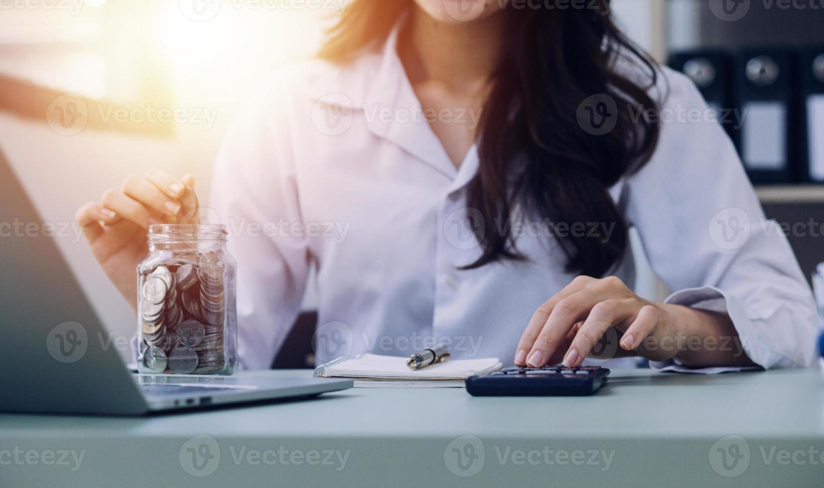 Young business woman sitting in office at table and using smartphone. On desk is laptop and tablet computer, on screen charts and graphs. Woman analyzing data. Student learning online. photo