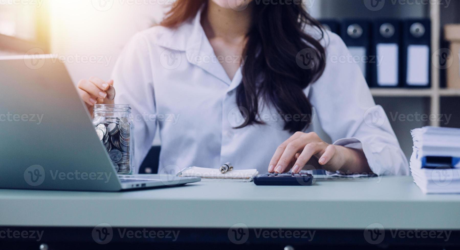 Young business woman sitting in office at table and using smartphone. On desk is laptop and tablet computer, on screen charts and graphs. Woman analyzing data. Student learning online. photo