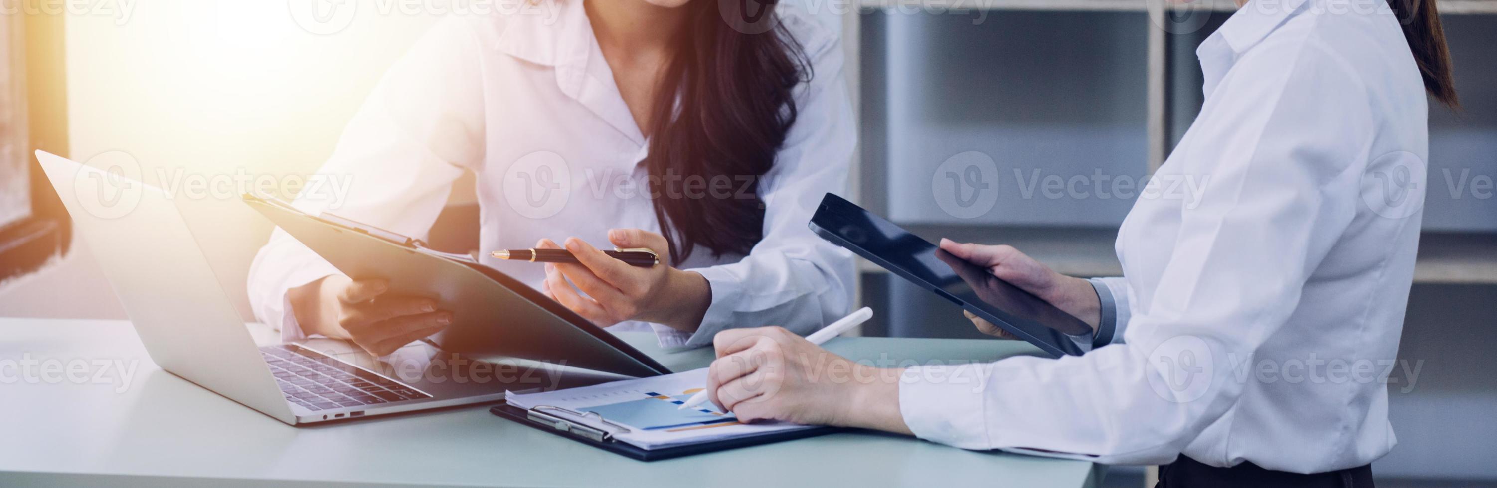 Young business woman sitting in office at table and using smartphone. On desk is laptop and tablet computer, on screen charts and graphs. Woman analyzing data. Student learning online. photo