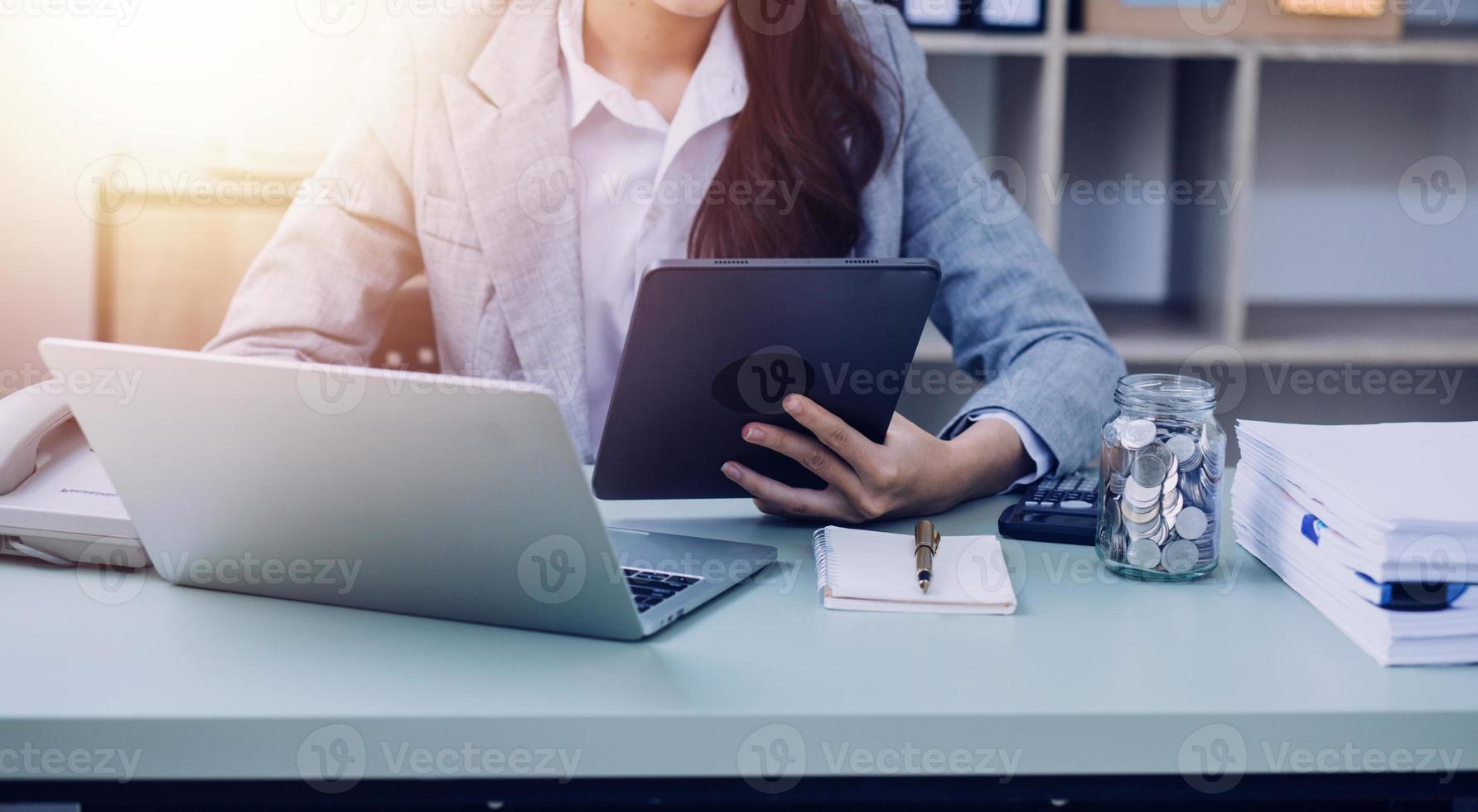 Young business woman sitting in office at table and using smartphone. On desk is laptop and tablet computer, on screen charts and graphs. Woman analyzing data. Student learning online. photo