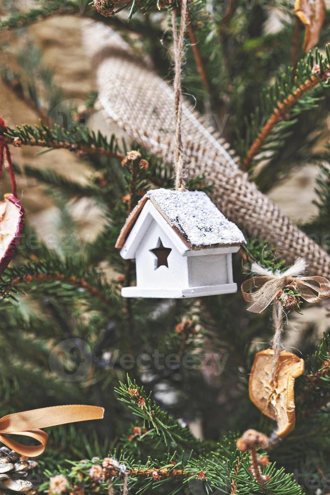 casa de juguete de madera vintage en el árbol de navidad. adornos navideños naturales para el árbol de navidad, cero desperdicio foto