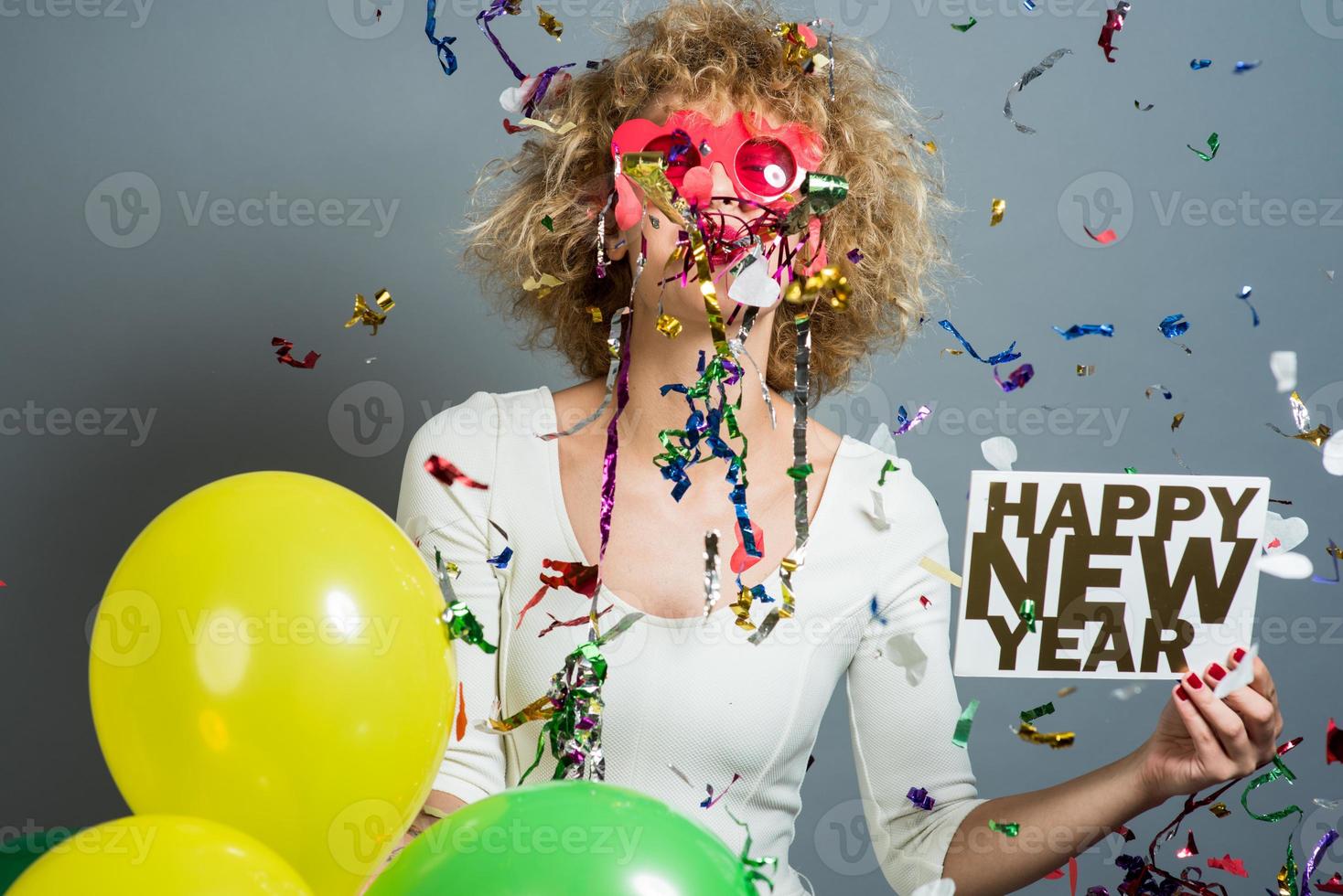 Beautiful woman celebrating New Year with confetti and holding sign. photo