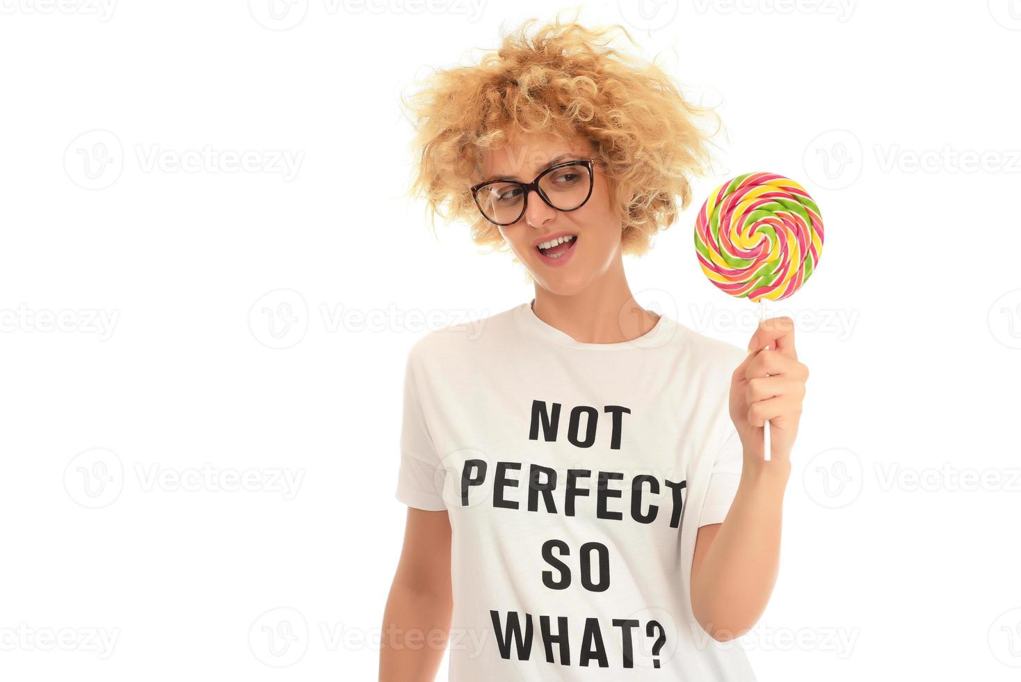 Blonde woman licking sweet candy. Female model eating delicious confectionery lollipop with surprised expression. photo