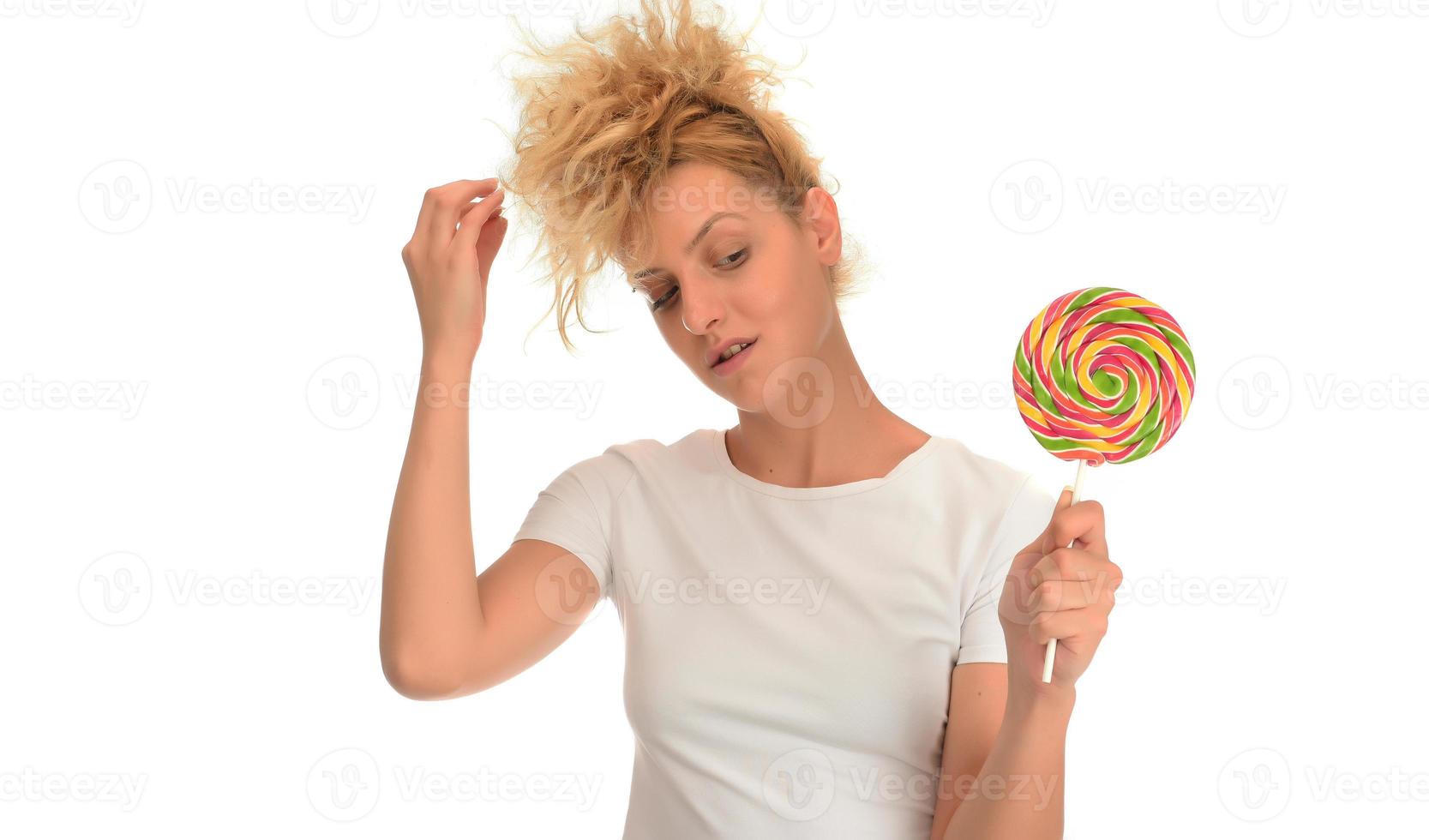 Blonde woman licking sweet candy. Female model eating delicious confectionery lollipop with surprised expression. photo