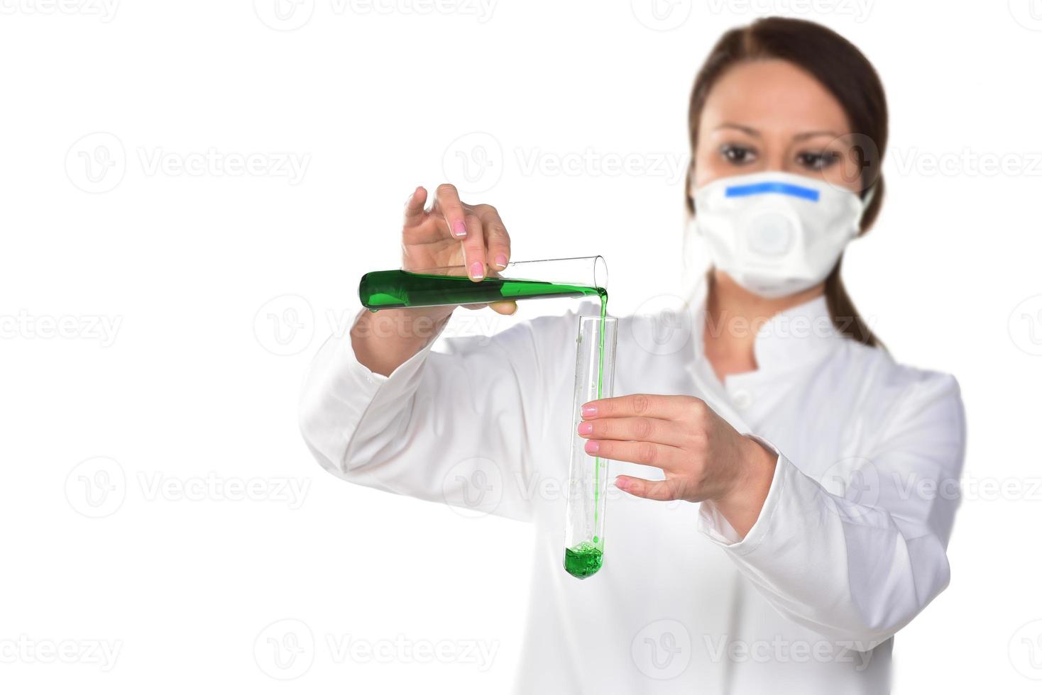 Scientist with white mask holding two tubes transferring green liquid from one to another. photo