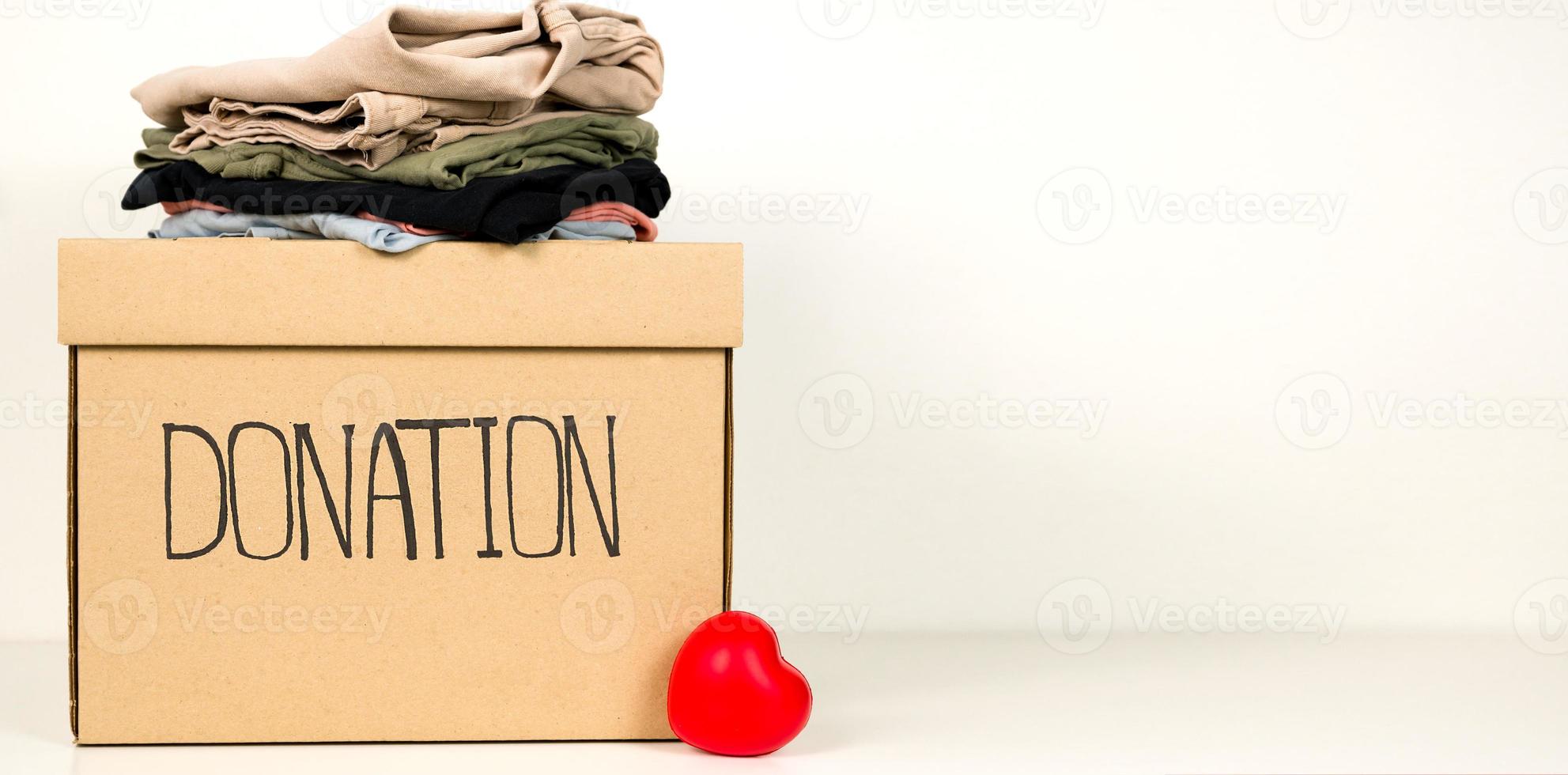 Charity concept copyspace banner. A box with pile of clothes against whote background photo