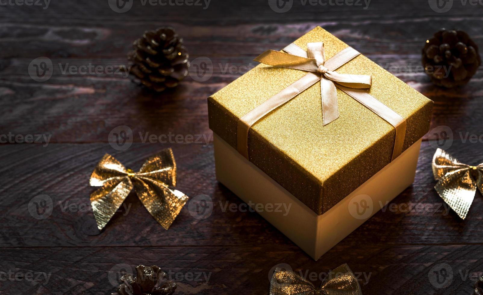 primer plano de una caja de regalo dorada brillante sobre una mesa de madera con arcos y conos cerca. banner de navidad o año nuevo foto