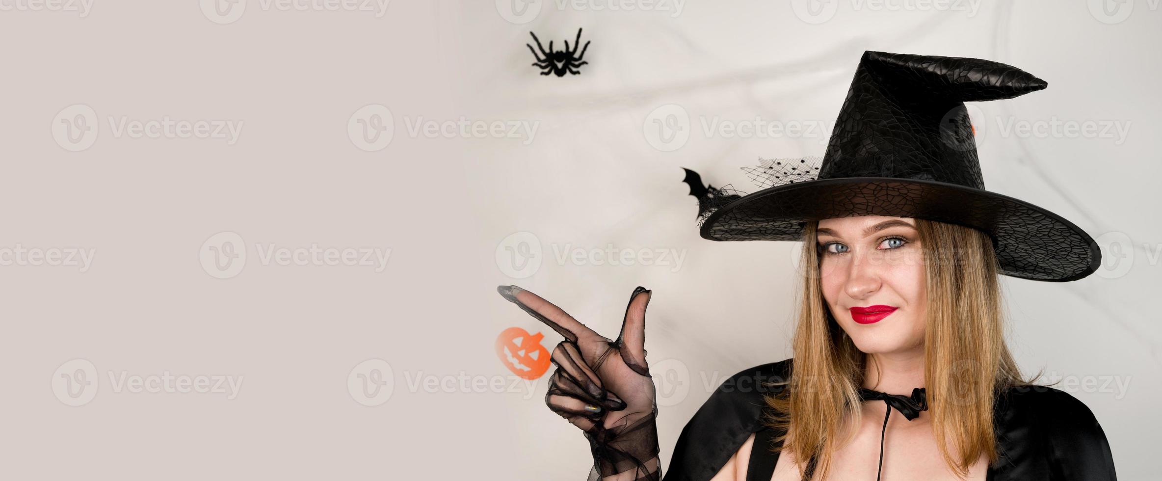 Halloween copyspace banner with beautiful blonde in a witch costume pointing at empy space.Party invitation. photo