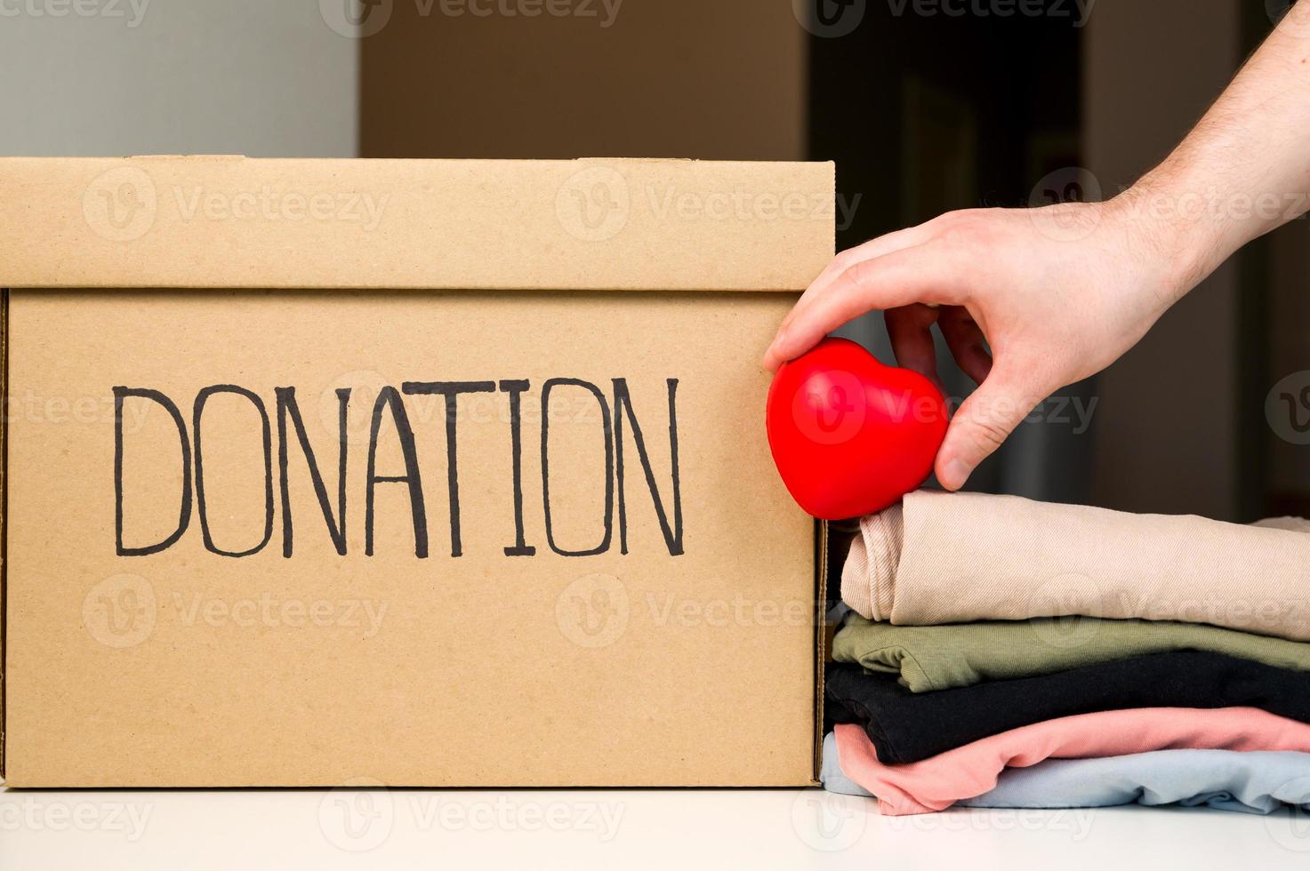 Unrecognizable male holding heart near donation box and stack of clothes. Helping people. Charity photo