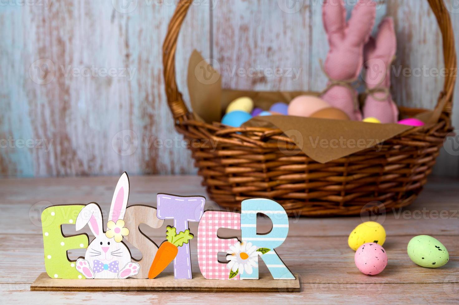 Easter wooden sign stads against easter basket with eggs and toy bannies.Happy easter banner photo