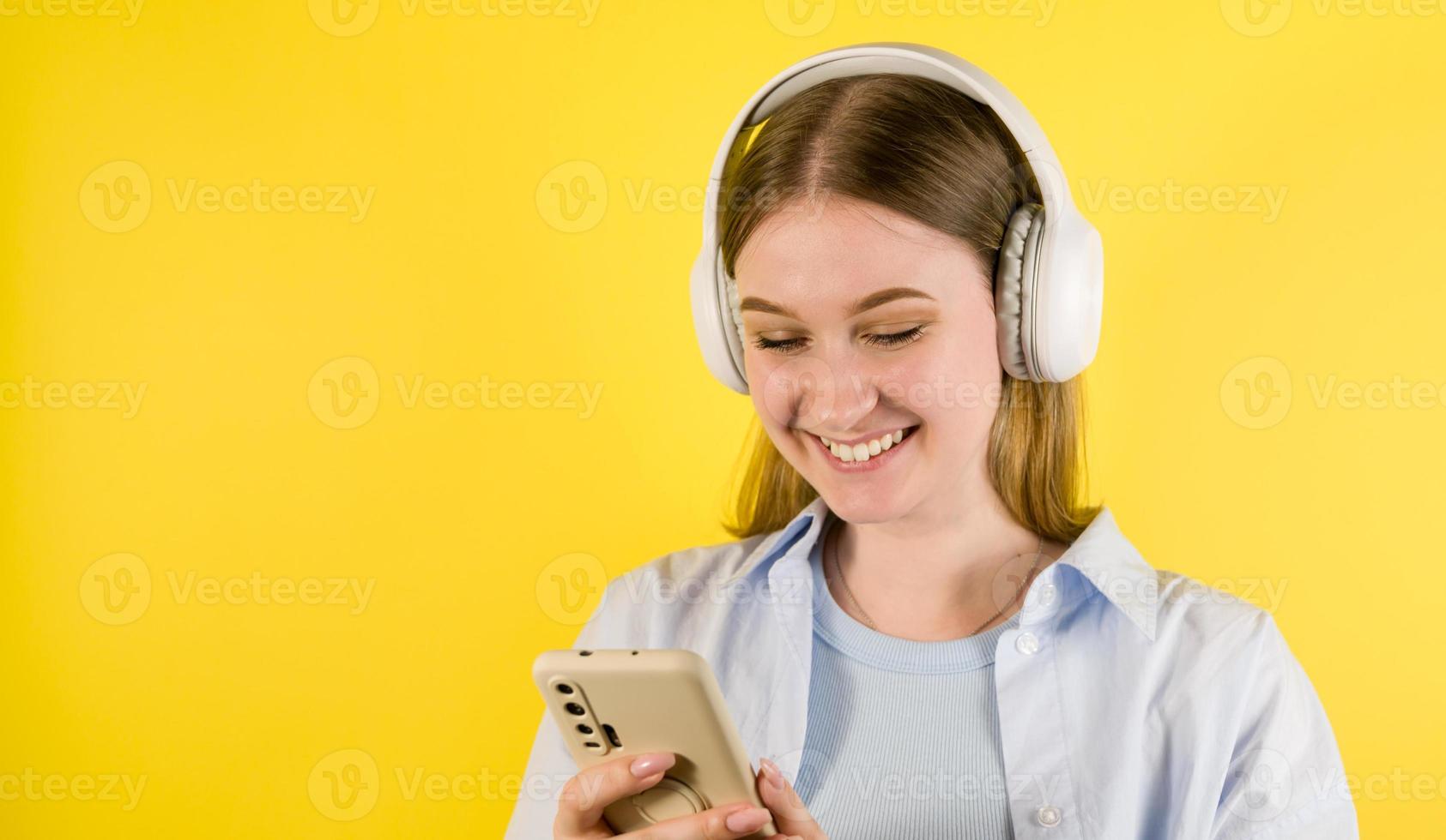 retrato de primer plano de un joven estudiante feliz con auriculares usando un teléfono inteligente. Aplicación para idiomas. Escuche podcast, música. Uso de medios sociales Retrato de estudio. De vuelta a la escuela foto