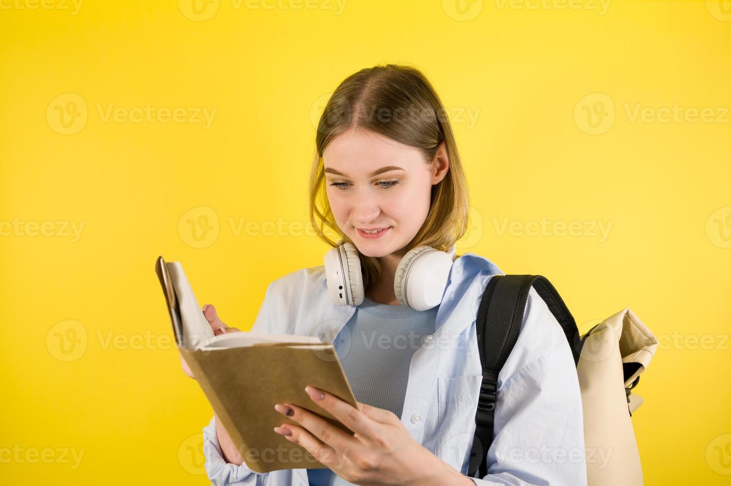 Cheerful young student girl in blue shirt with backpack reading book. Education in high school university college concept. Copyspace banner photo