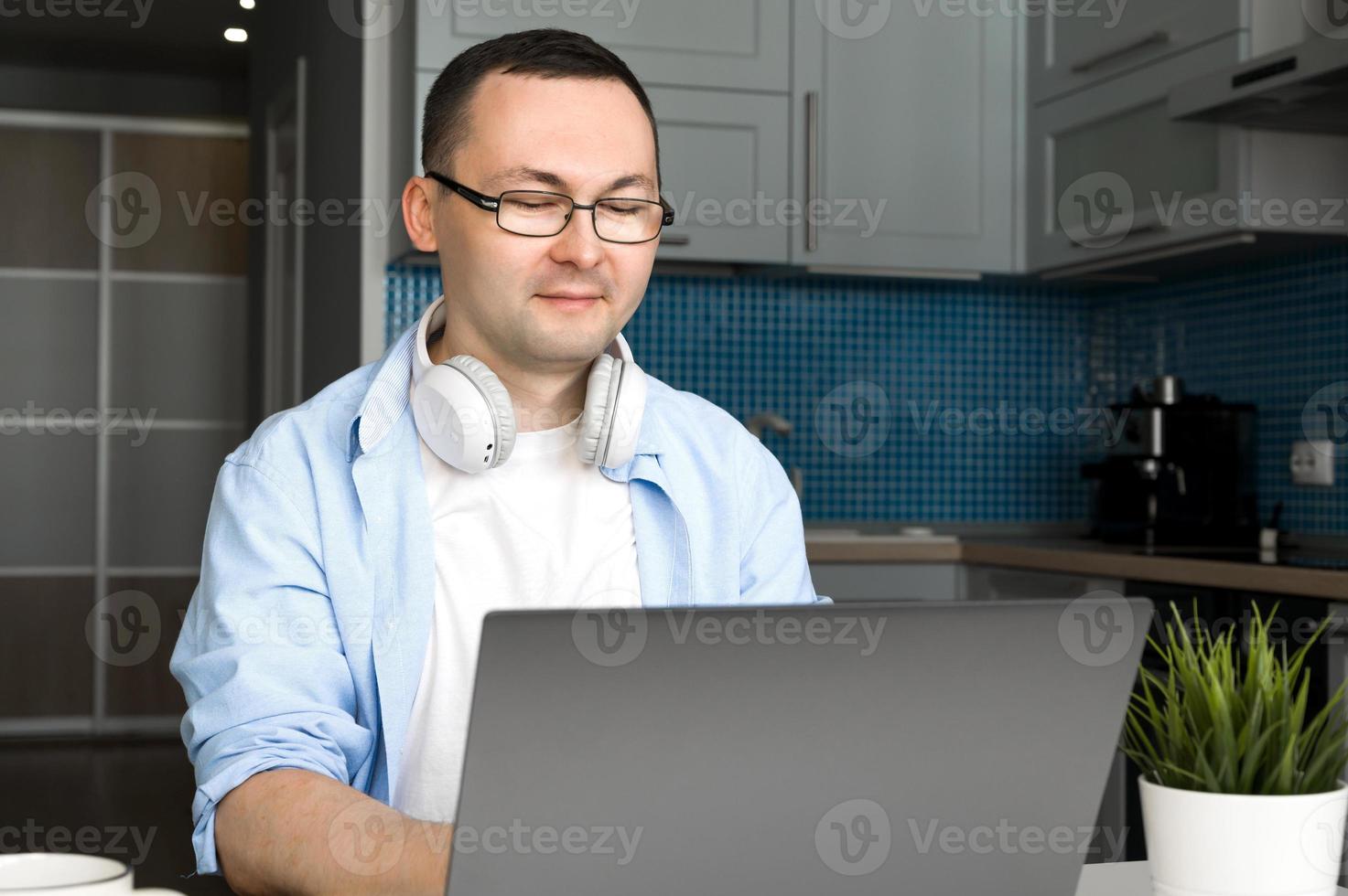 Asian smiling male in glasses uses laptop for shopping,programming,working etc.Modern technologies concept photo