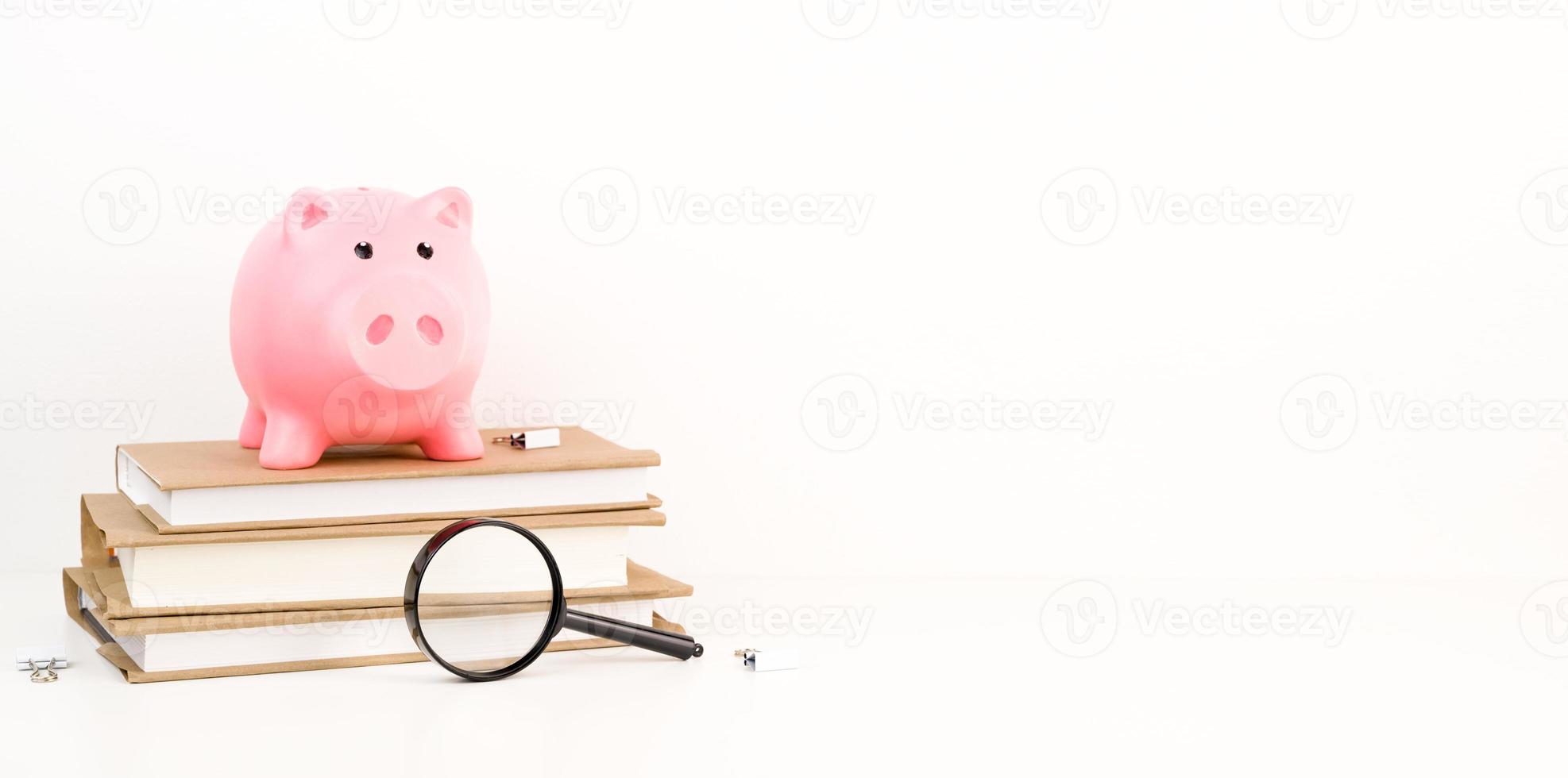 Closeup of Pink Piggy bank on top of books with magnifier as concept of the cost of education or research. Education or research fund.Scholarship concept.Banner with place for text photo