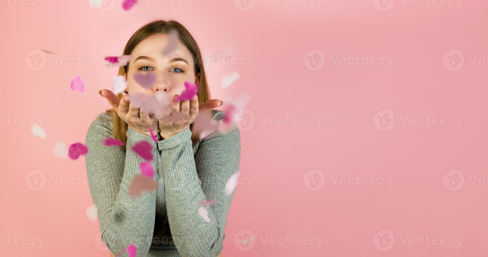 Studio portrait of a young happy female blowing heart shaped confetti. St Valentine's day concept copyspace banner photo