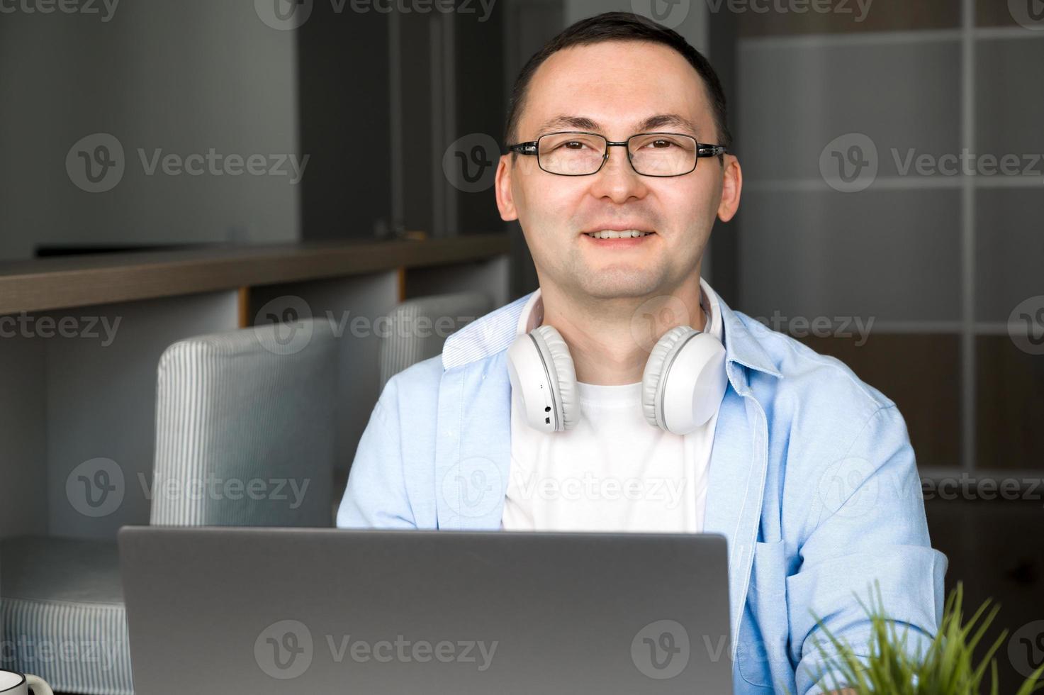 Happy asian man smiles at camera while sitting behind laptop. Modern technologies concept. photo