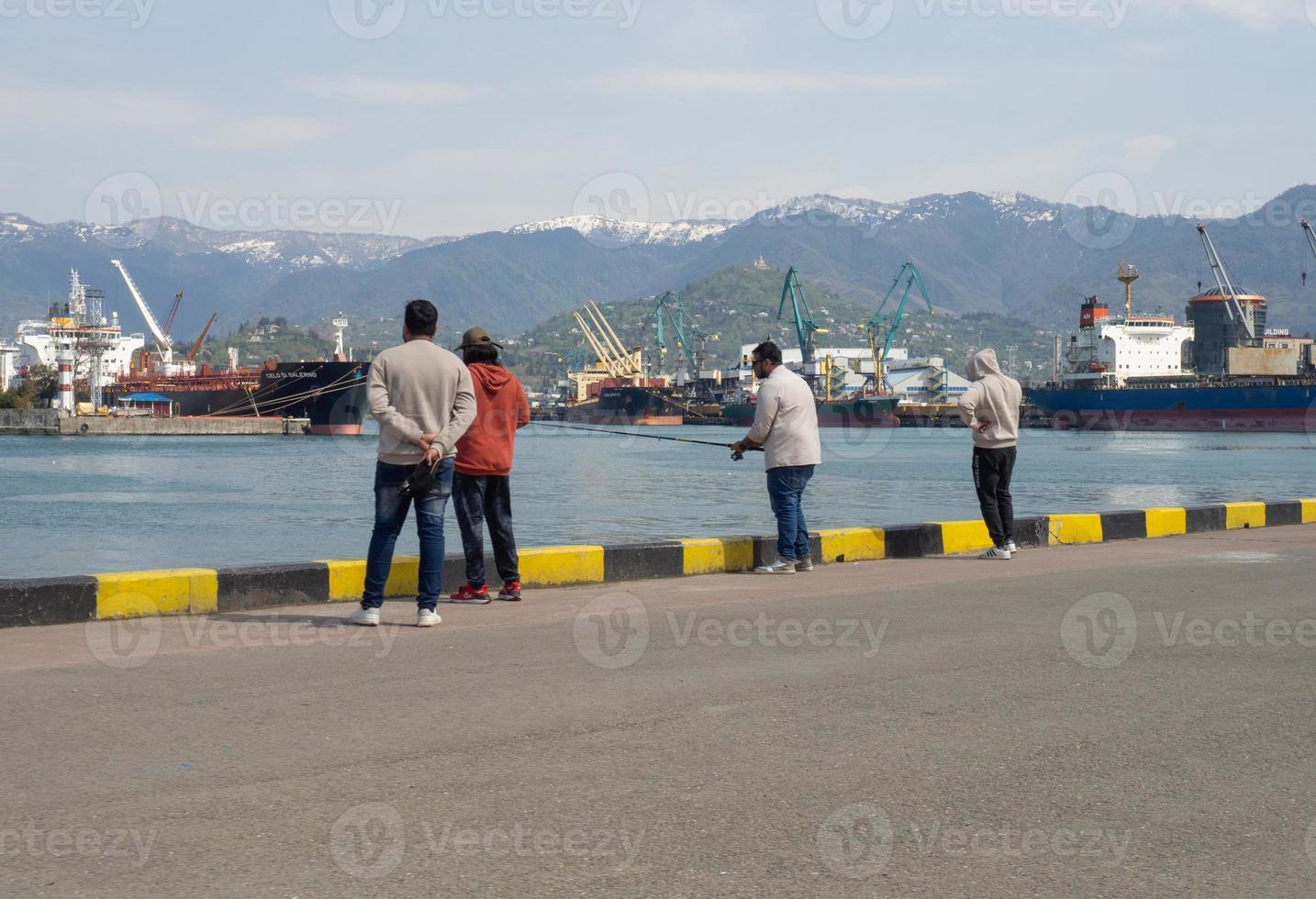 Fishermen with fishing rods on the mooring of the city port. On the sea coast. photo