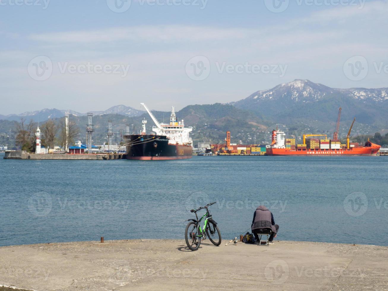 Fisherman on a bike  on the pier on the seashore.  A man is sitting on the beach with a fishing rod. photo