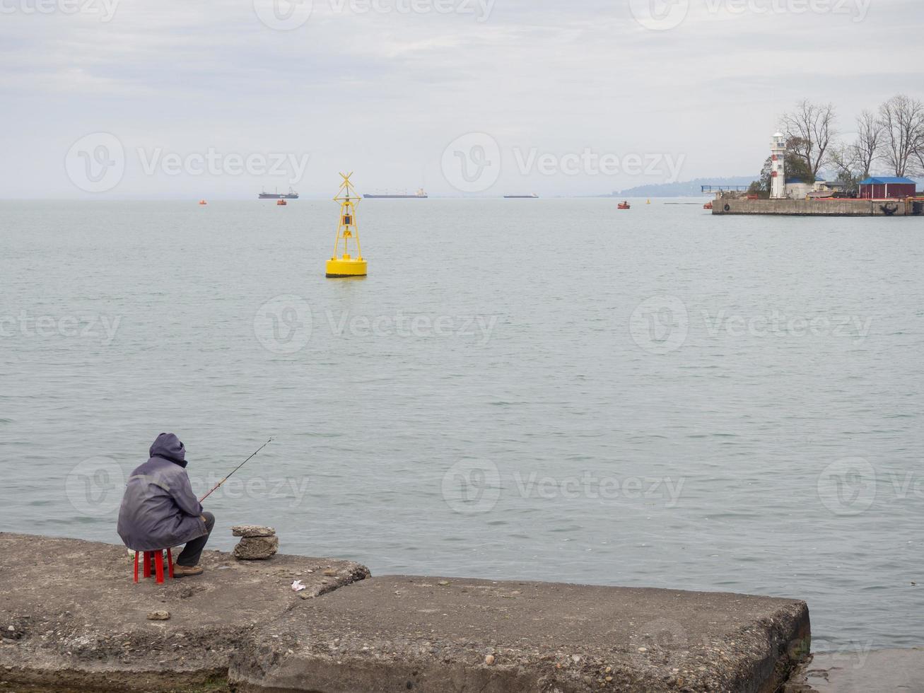 Fisherman on the pier on the seashore. A man is sitting on the beach with a fishing  rod. 15190354 Stock Photo at Vecteezy