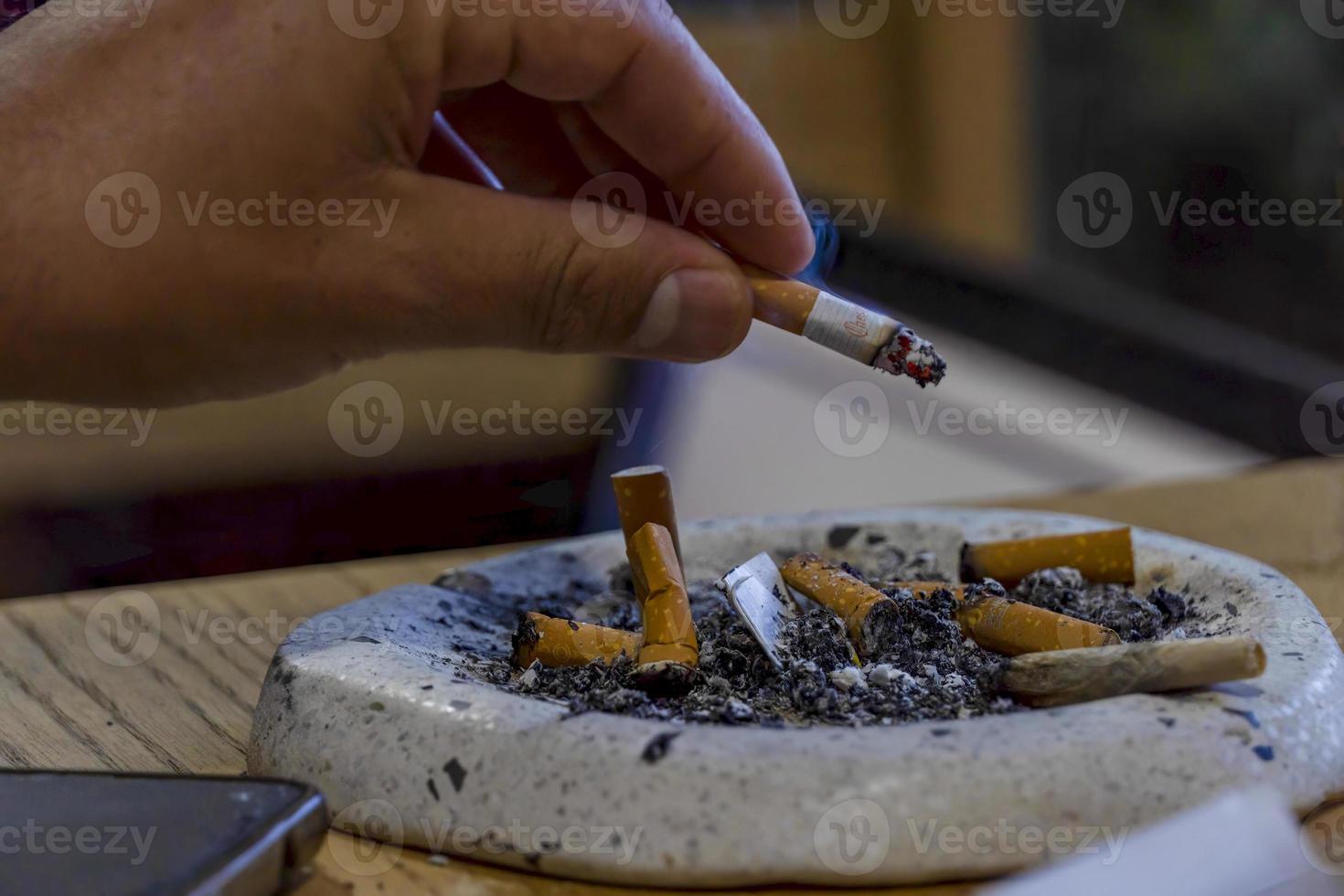 young man smoking on a wooden table, ashtray with several used cigars, mexico photo