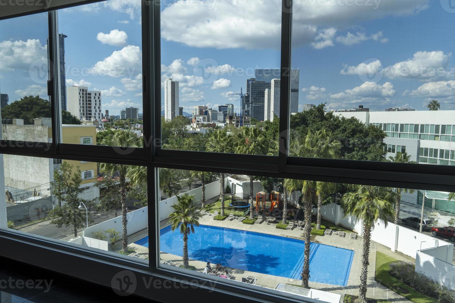 view of a swimming pool from an apartment up in a tower, view of buildings, trees and palm trees photo